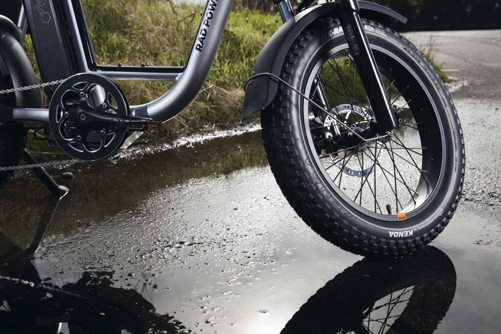 A close up of a tire attached to a silver electric bike on wet pavement471122340 1 1