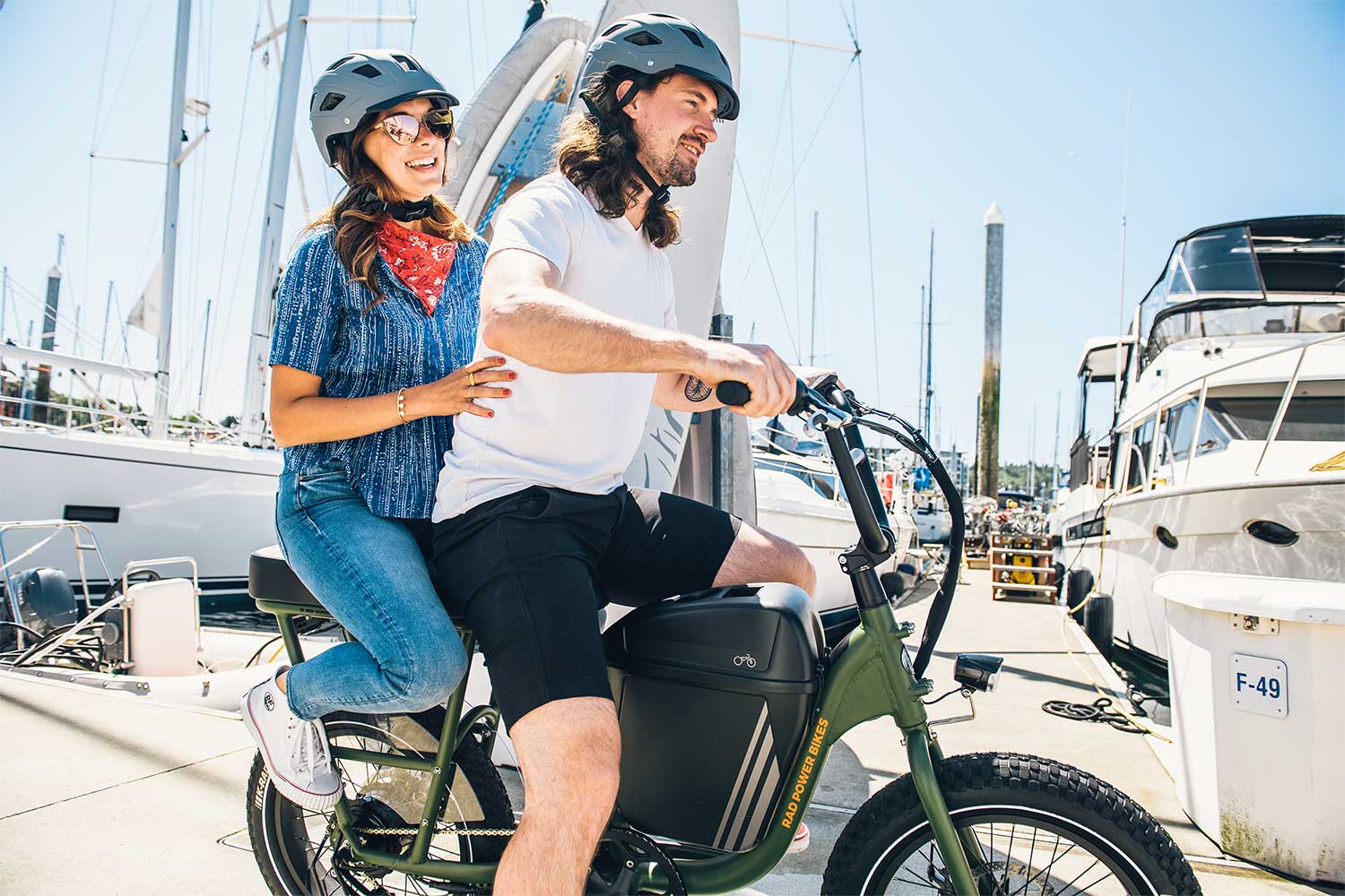 A woman and mad ride the RadRunner, 2021's best utility ebike,on. a dock.