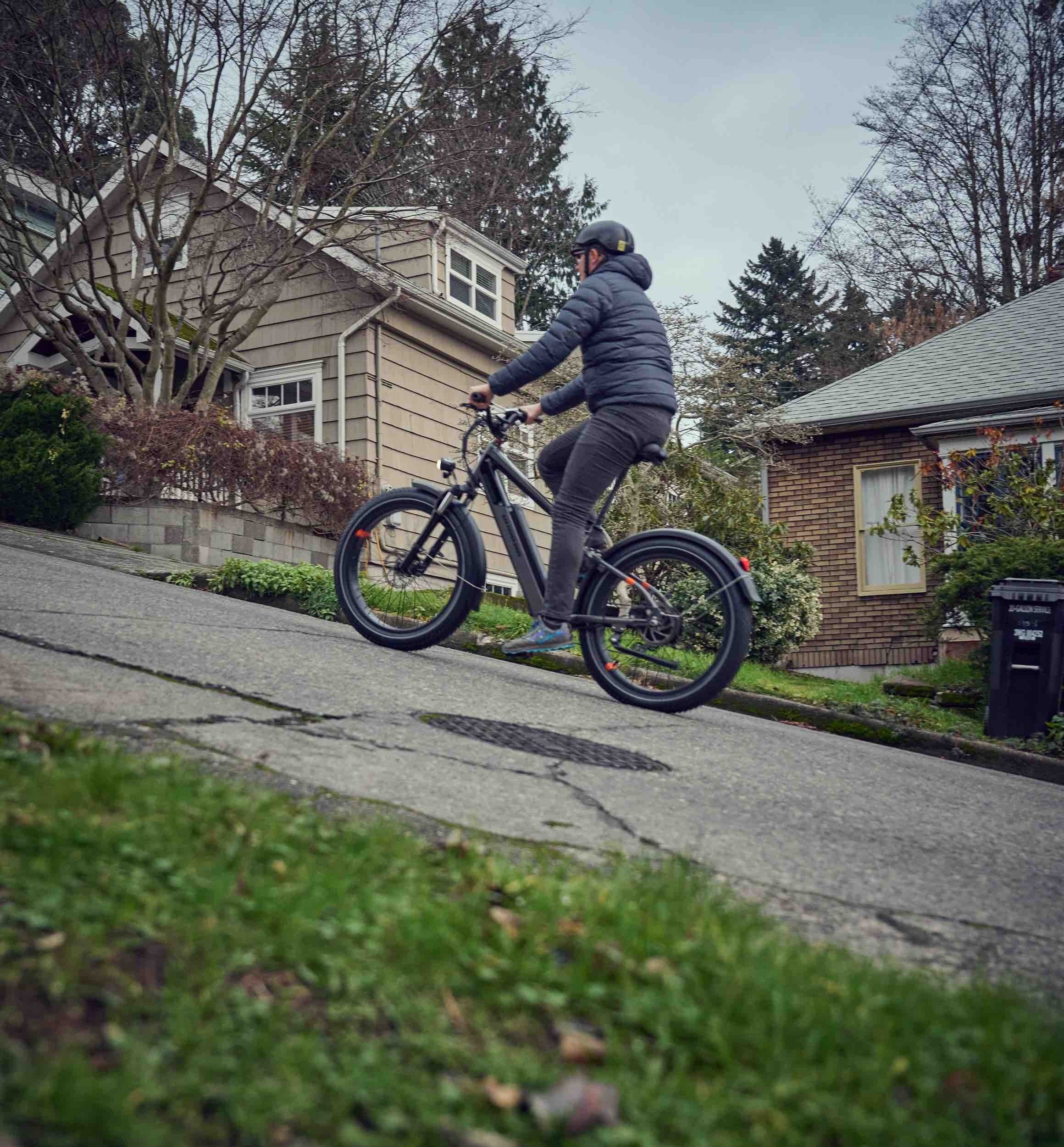 Man rides on Rad Power Bike black ebike up a steep incline.