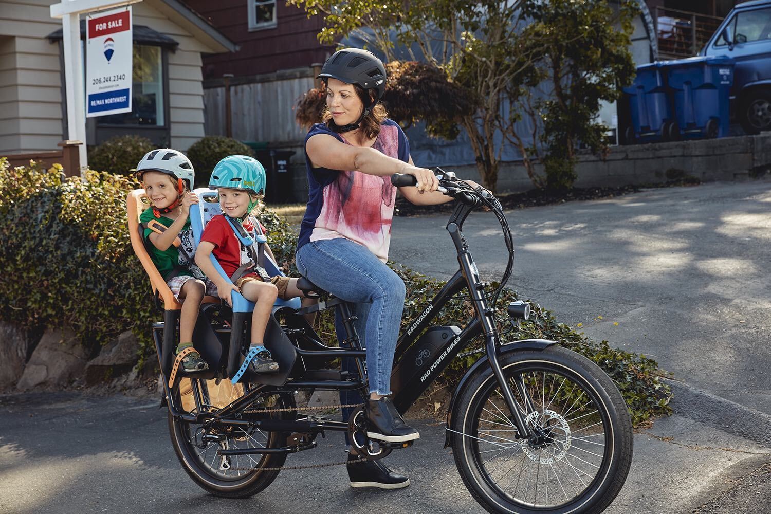 Mother rides a cargo electric Rad Power Bike RadWagon with two children behind her.